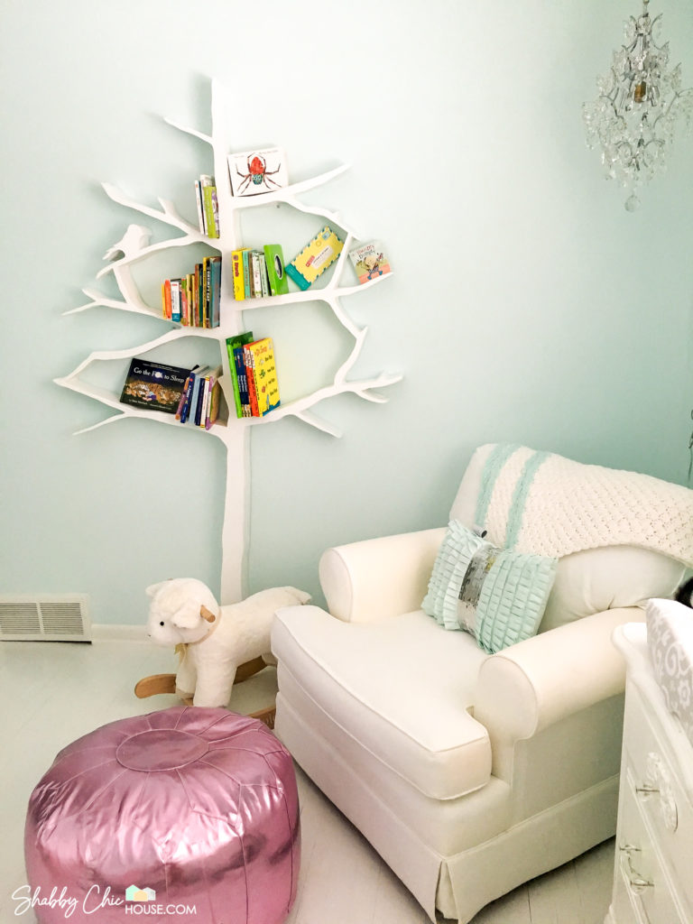White Tree Shaped Bookshelf filled with books next to lamb rocking horse, baby room rocking chair and pink poof