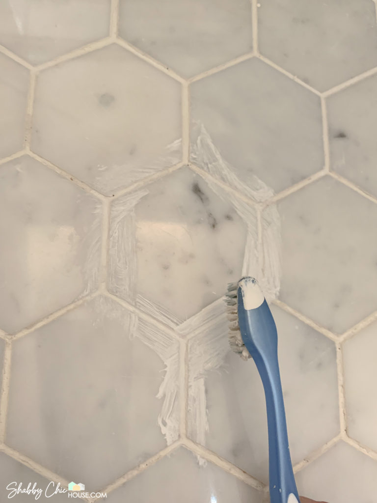 Using a Toothbrush to apply white paint grout and restore stained grout