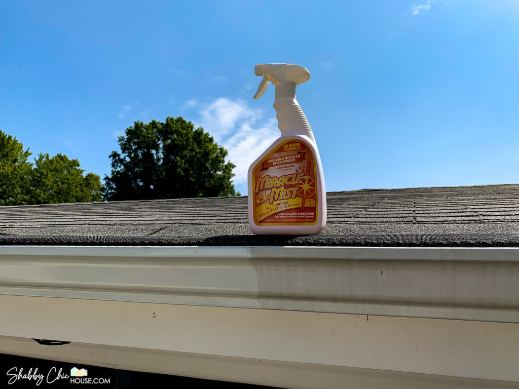 shot of a bottle of Miracle Mist on a rooftop above a gutter where the left have is bright white and clean and the right half if dirty and gross with grime that has built up over time.
