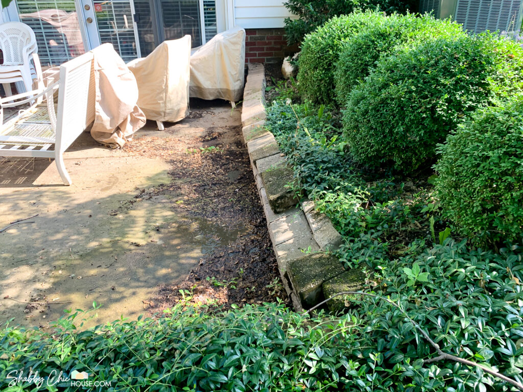 photo of a gross and dirty patio in need of cleaning and it's small retaining wall that is falling over due to erosion.