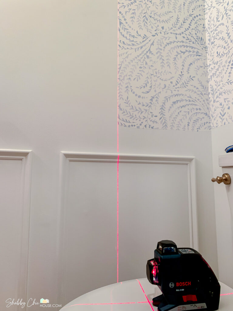 Bosch laser level being used to set the plumb line when hanging wallpaper