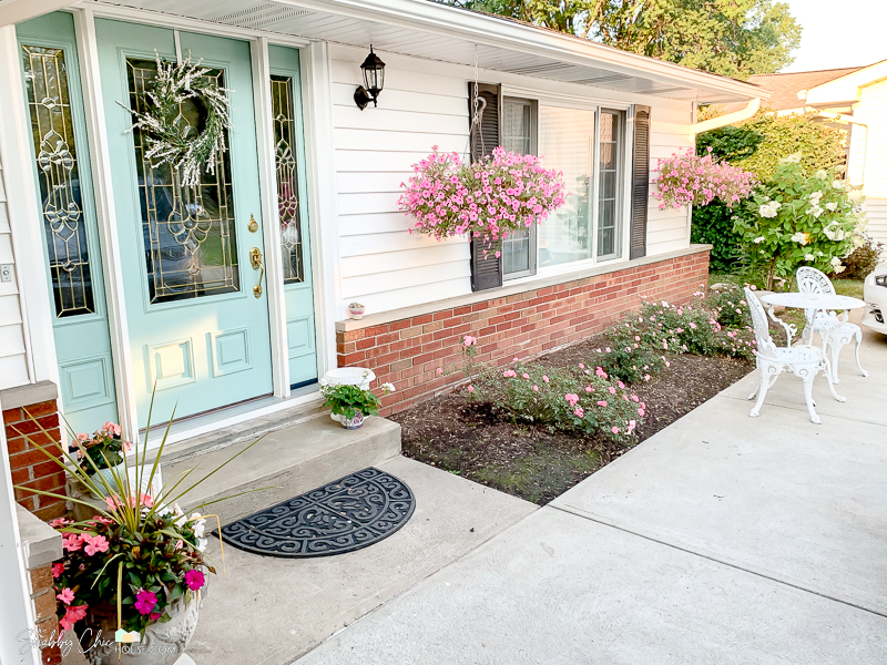 landscaping upgraded to add color to the front of a monochromatic house and boost curb appeal. Numerous planters with shades of pink flowers, two hanging baskets, pink and peach knockout roses and a Peegee hydrangea tree.