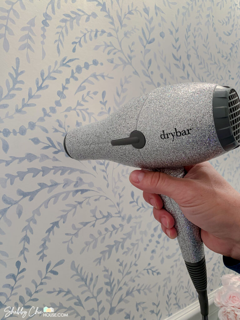 Photo of a sparkly hair dryer being used to warm the wallpaper where there is an air bubble stuck underneath. Just warm air bubble for 2-3 minutes, occasionally working with a smoothing tool until gone.
