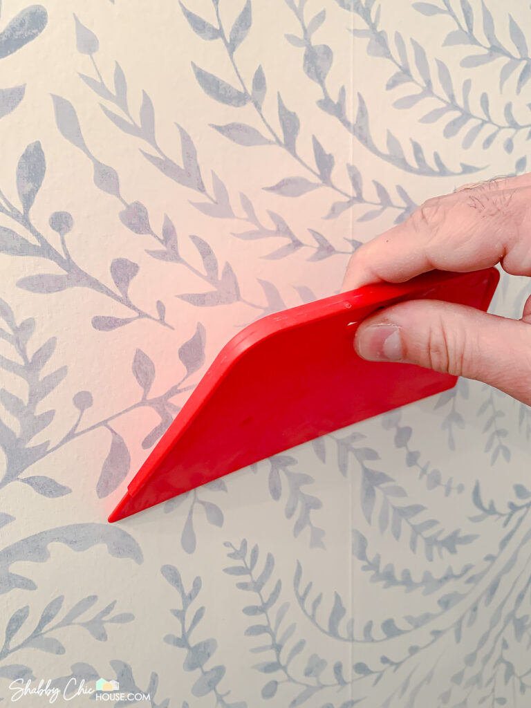 Using a red smoothing tool right after hanging a piece of wallpaper to smooth out the paper and remove air bubbles