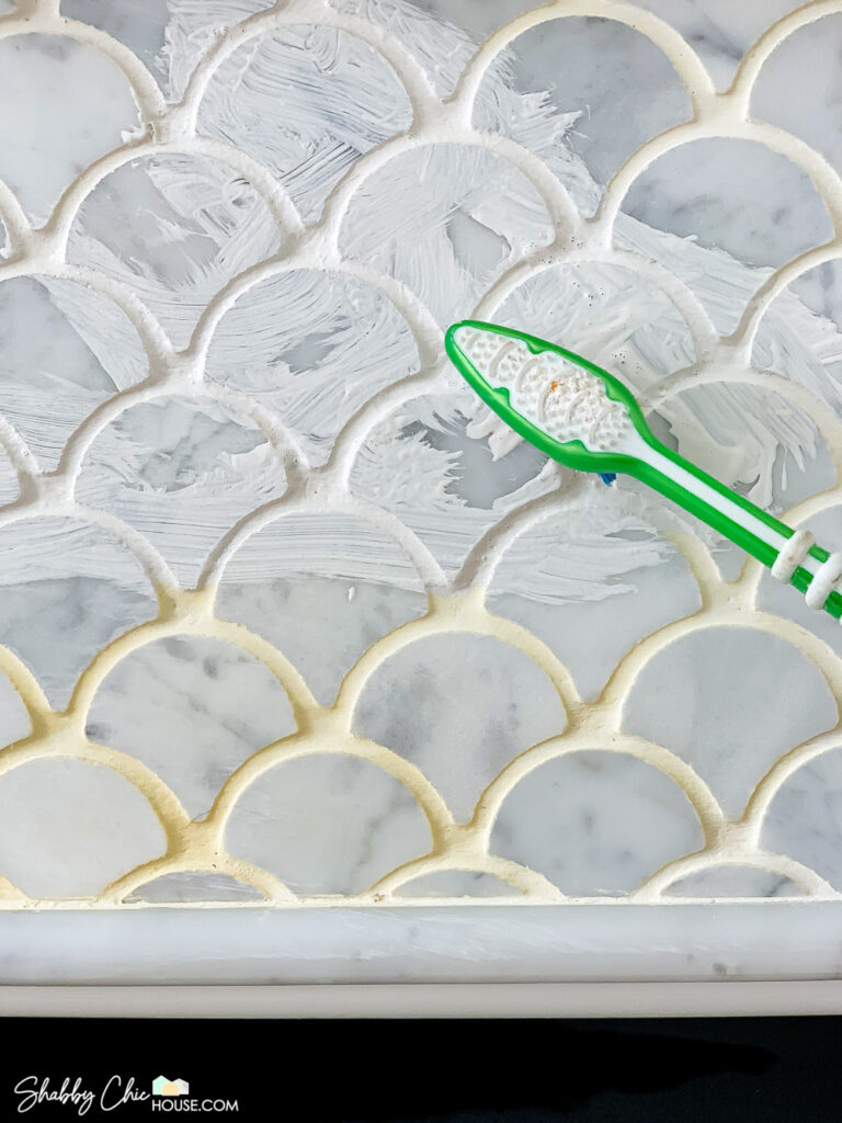 Applying a white grout colorant by Mapei with a toothbrush to clean and refresh white tile grout on a fireplace surround that has been discolored by heat