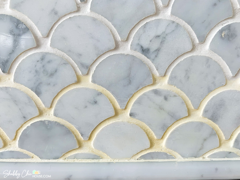 Close-up of white grout on a fireplace tile surround. Top tile grout has been cleaned / refreshed and painted white. The bottom half of the photo has tile grout that is yellow and stained prior to Mapei grout colorant.
