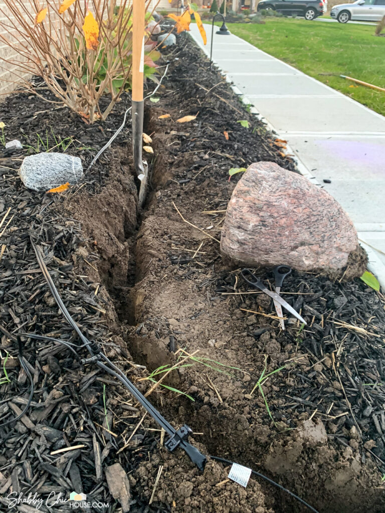 Digging a 6" deep trough to run low voltage electrical wiring for a DIY landscape lighting project.