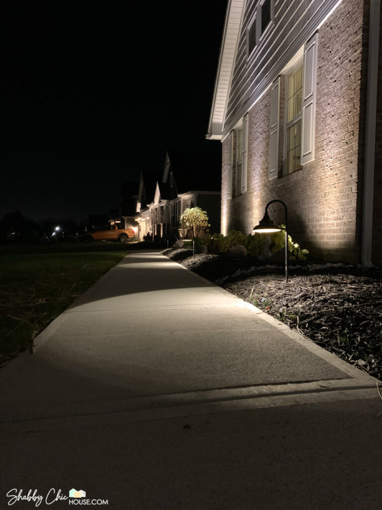 Ground show showing pathway lighting the sidewalk in front of a house as well as uplighting on the brick house and a small ornamental tree.