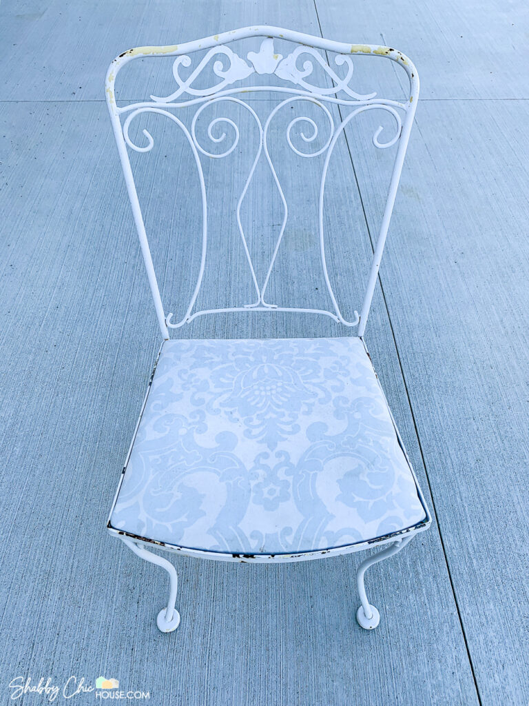 تصویر یک صندلی فرفورژه تکی، ضربه خورده توسط عناصر، زنگ زده و با رنگ پوست کنده قبل از تعمیر اساسی.