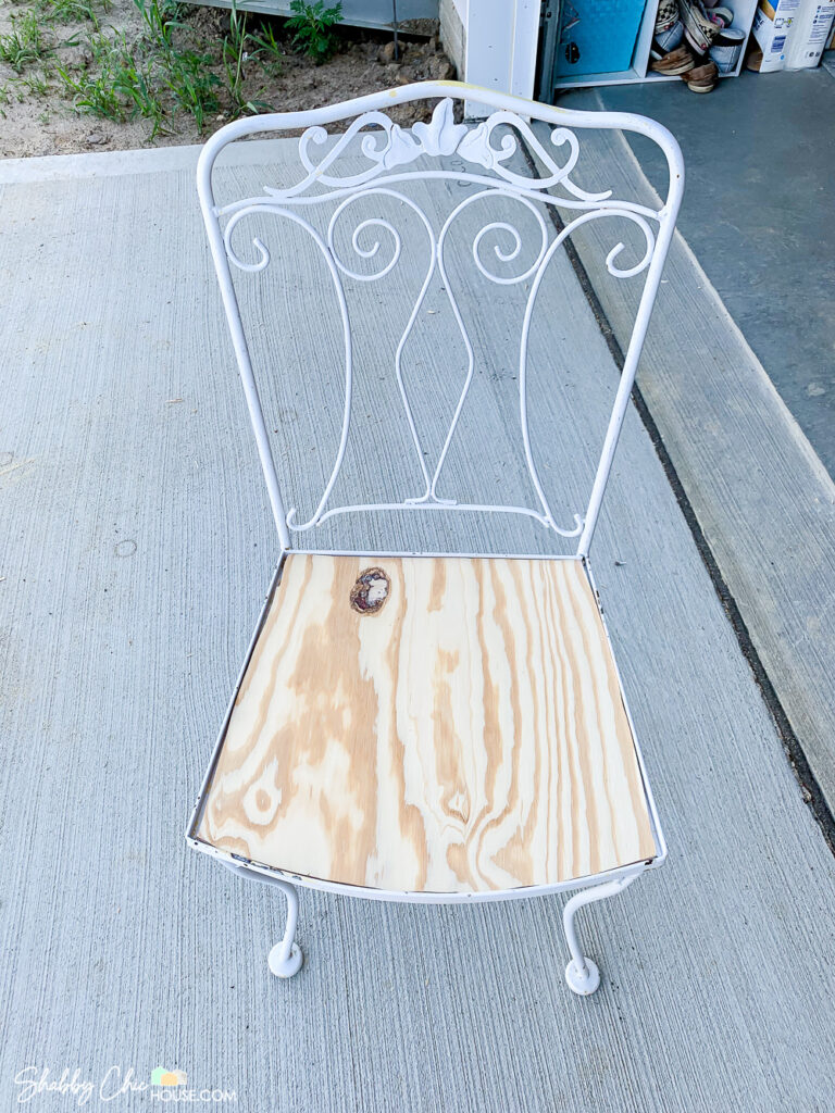 Image of a wrought iron chair and a piece of plywood that has been cut with a jig saw so a new foam cushion can be and fabric can be installed.