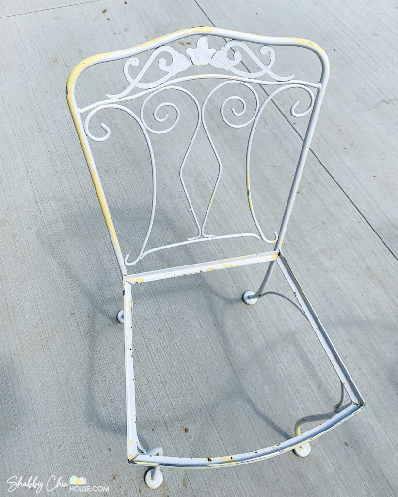 Image of a wrought iron chair that is being restored. Rusty areas have been sanded down in preparation to have the chair primed and repainted white.