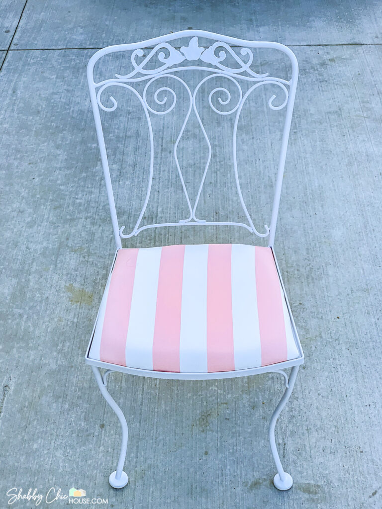 Single wrought iron chair of a wrought iron patio set that has been restored, repainted white and reupholstered with pink and white striped fabric.