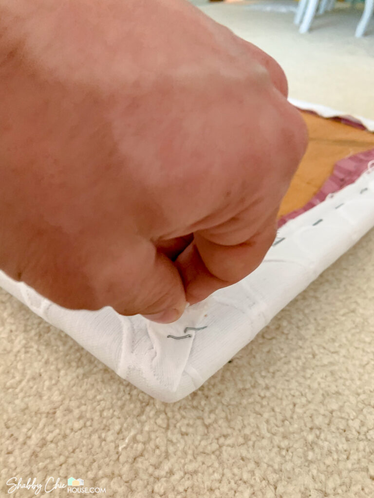 showing reupholstering a seat cushion and folding and stapling a pleat in the corner of the cushion.