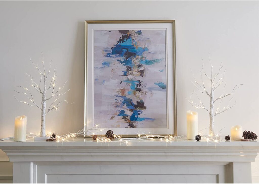 Image of two pre-lit birch tree home decor items on a fireplace off Amazon.com for a blog post on the top Christmas decorations ideas of 2021.