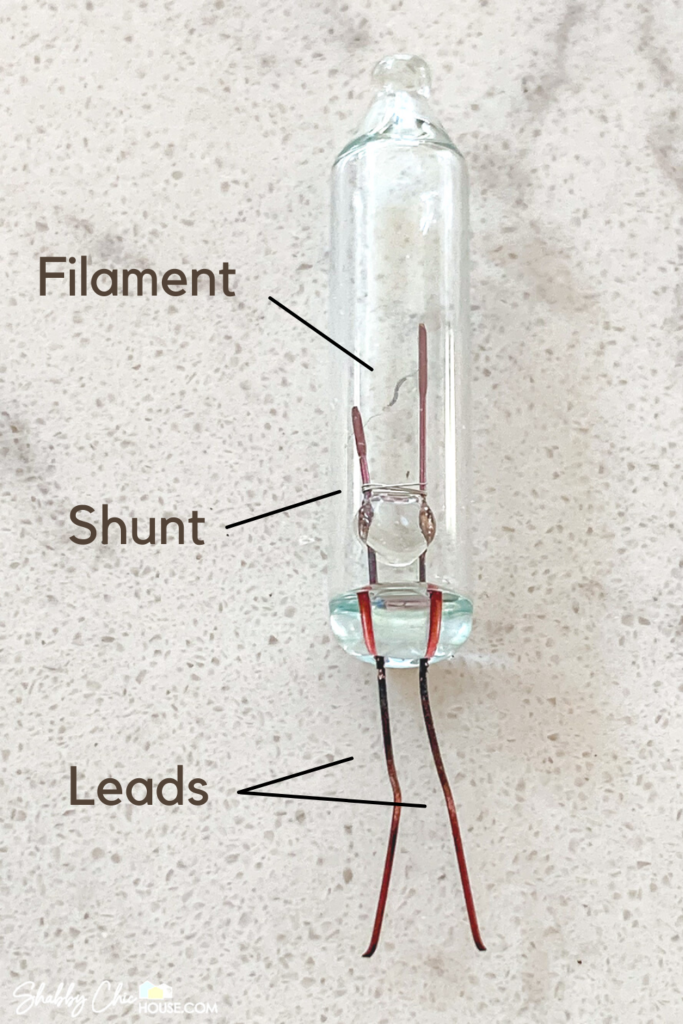 Close-up photograph of a Christmas light bulb that has been removed from its base. We can see the internal components of the bulb including the filament, shunt as well as the leads or prongs.