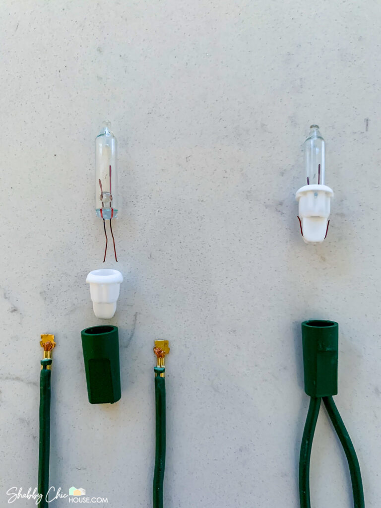 Photograph showing a dissected strand of Christmas tree lights. It shows the wiring and connector plates, the bulb, bulb base as well as the bulb socket to help demonstration how to fix broken Christmas lights.