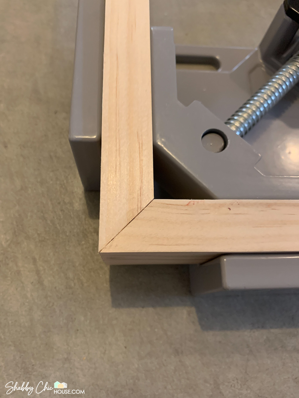 Close-up of a perfect miter for a DIY floating picture frame in a 90-degree wood working clamp.