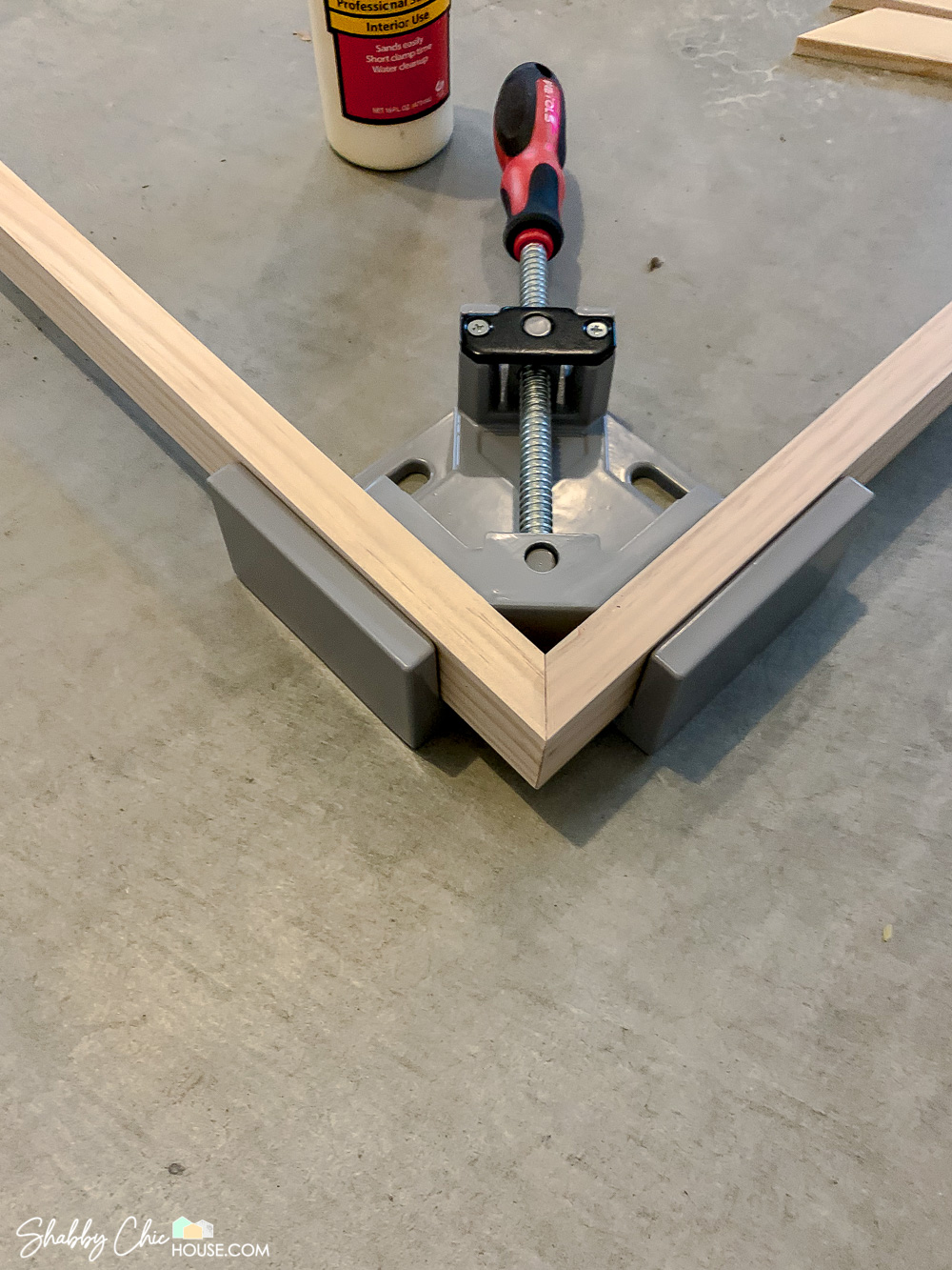 Close-up of a 90-degree wood working clamp being used to build a wooden DIY Floating Picture Frame.