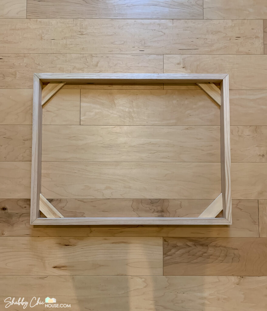 Picture of a wooden DIY floating picture frame made from 4 mitered 2x1's with 90-degree braces on the back.