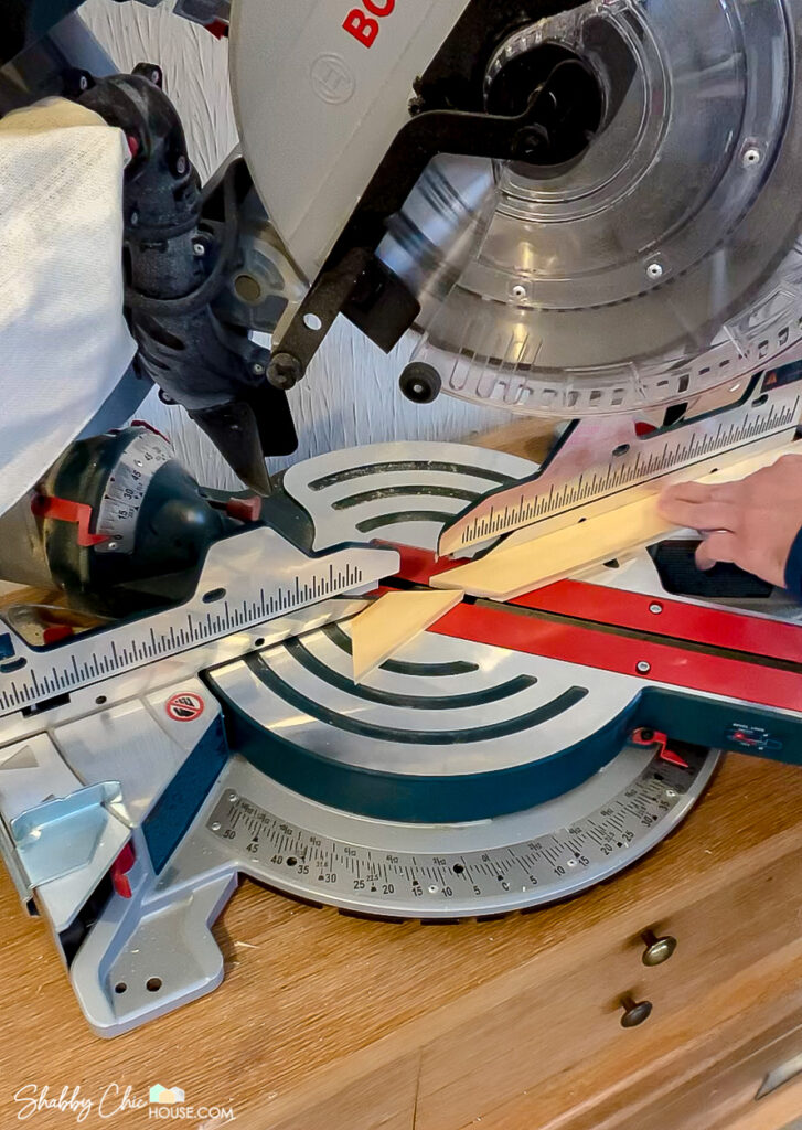 Close-up showing the braces being cut on a miter saw for the back of a DIY floating picture frame.