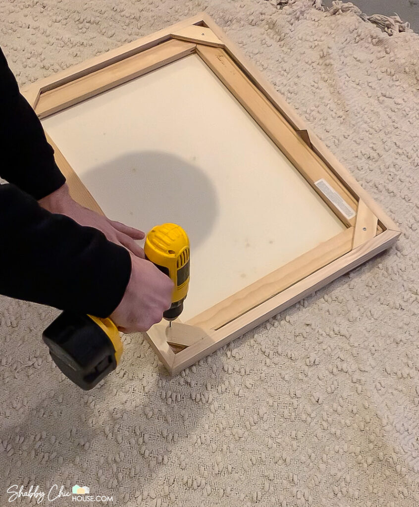 Image showing how to secure a canvas painting into a homemade wooden floating picture frame with screws.